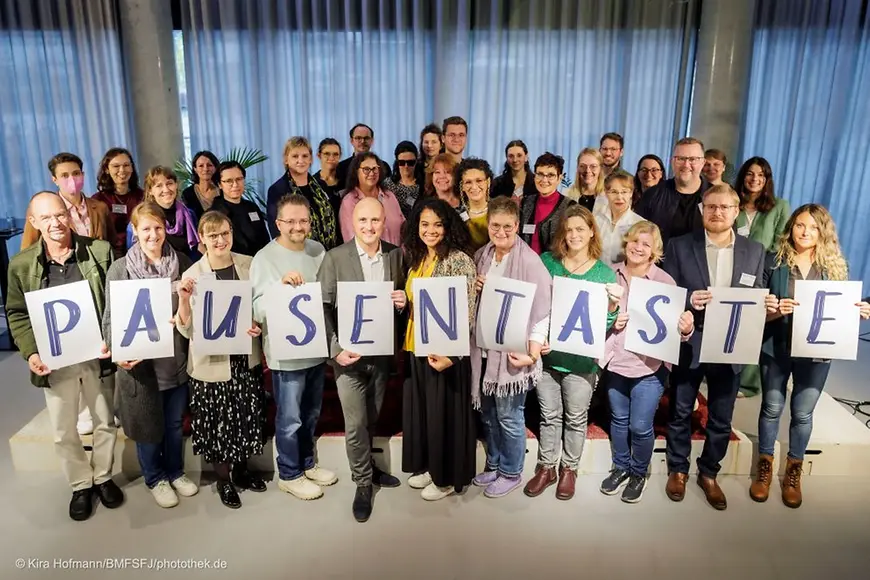 Gruppenfoto, Menschen halten Buchstaben hoch die das Wort "Pausentaste" ergeben
