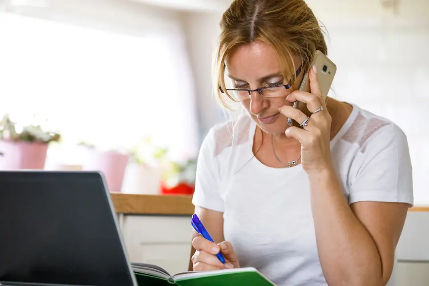 Eine Frau sitzt am Schreibtisch und ist am Telefonieren.