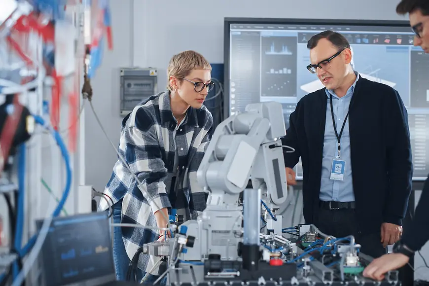 EIn MAnn und eine Frau stehen in einem Labor und beugen sich über eine Roboterhand